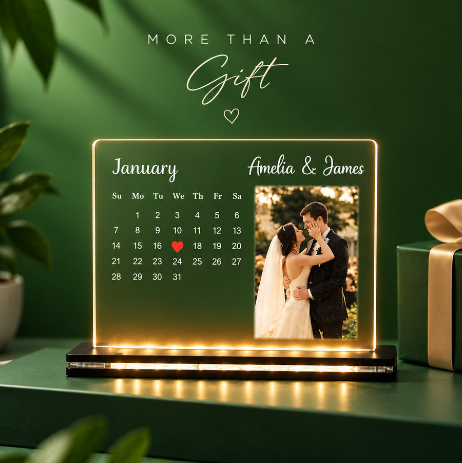 A personalized acrylic calendar gift box with warm LED lighting, displayed on a dark green table. The calendar shows 'January' with a date grid and a custom photo of a bride and groom.